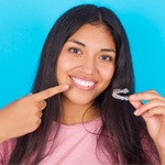 Teenage girl holding Invisalign and pointing to smile